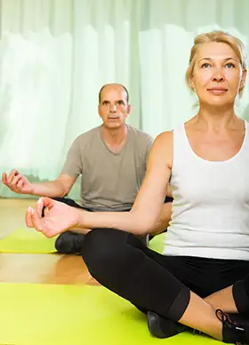 Casal na maturidade praticando técnicas respiratórias em aula de Yoga para terceira idade